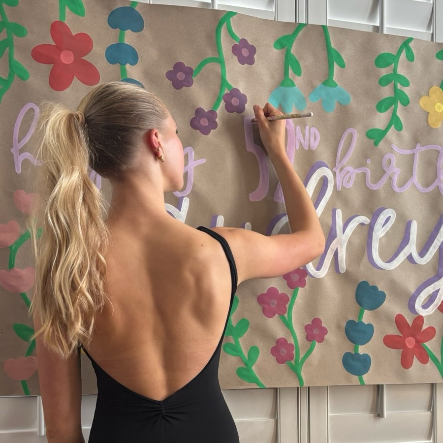 Mer hand-painting a large floral birthday banner on kraft paper