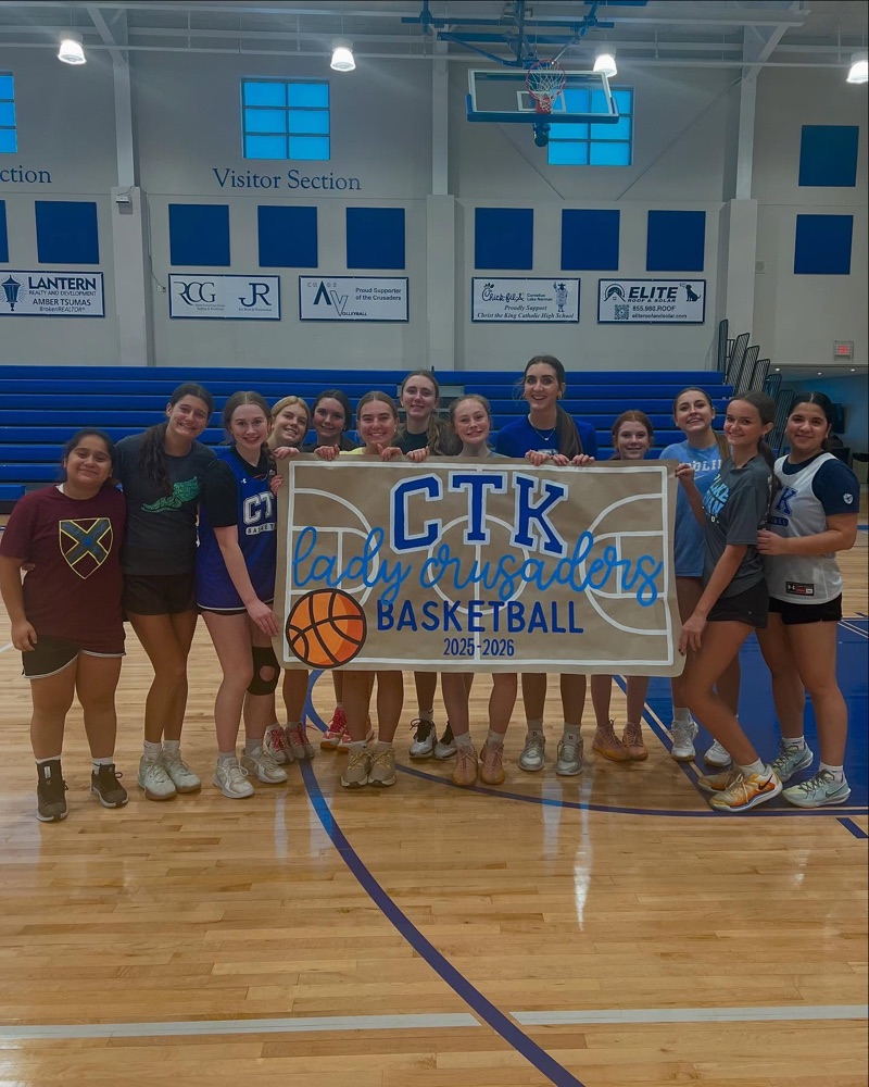 A girls basketball team holding a hand-painted CTK Lady Crusaders Basketball banner in a gym
